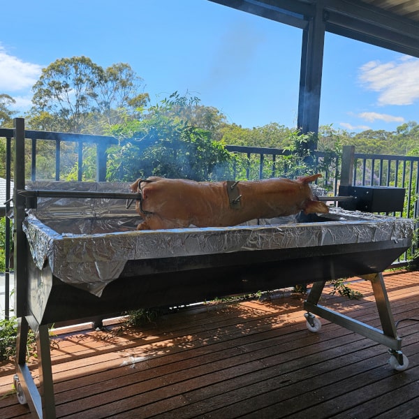 A full pig on a spit cooking over charcoal on a patio deck