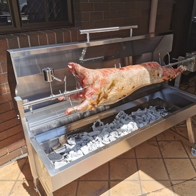 a whole lamb on a  1500 spit rotisserie cooking showing one of our hire cooks