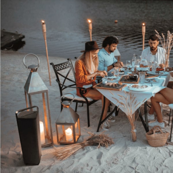 Outdoor bluetooth speaker next to a table of people eating ona  beach